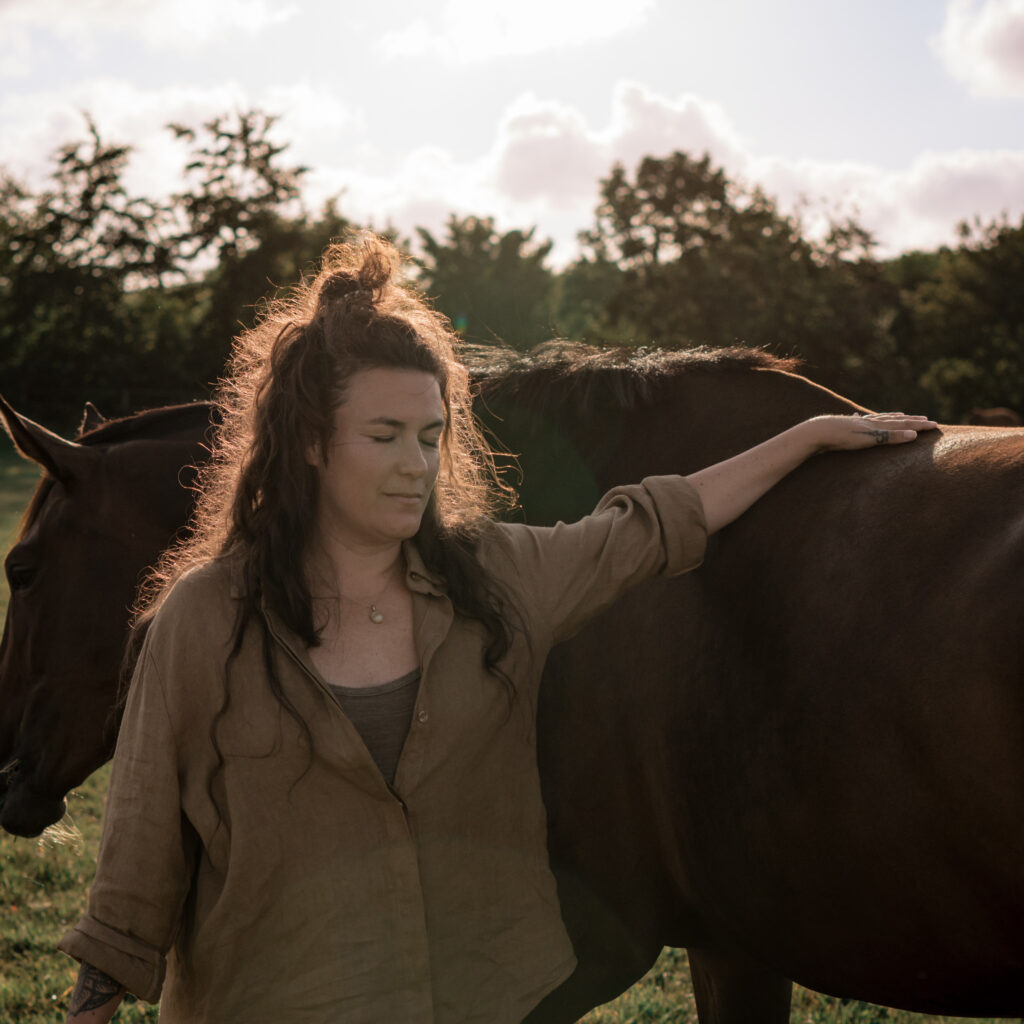 Portretfoto van Illja Bos waarbij ze haar hand op een paard legt